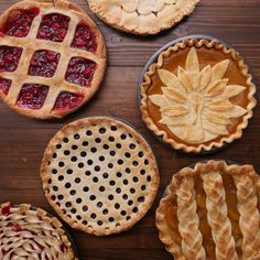 four pies with different toppings on top of a wooden table next to each other