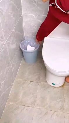 a person is cleaning a toilet in a bathroom with a bucket on the floor next to it