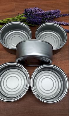 four tins sitting on top of a wooden table next to lavender sprigs