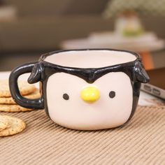 a penguin mug sitting on top of a table next to crackers