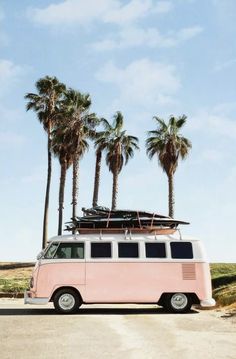 a pink van with surfboards on top parked in front of palm trees