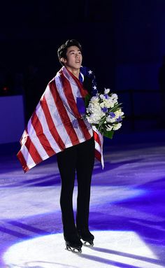 a man holding an american flag and flowers on top of a ice rink at night