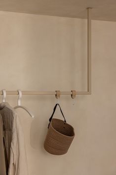 a basket hanging on the wall next to a coat rack with two hooks and a hat hanger