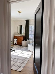 an open door leading to a bedroom with a bed and dresser in the background on a wooden floor