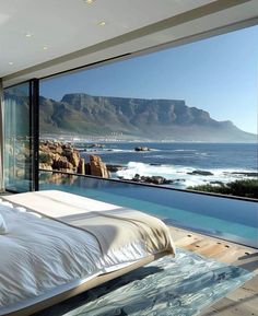 a large bed sitting next to a window overlooking the ocean and mountains in front of it