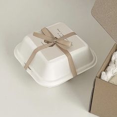 a white box with a brown ribbon around it and some tissue in the other side