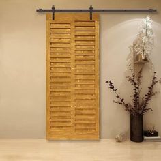 a room with a vase and wooden shutters on the wall next to a plant