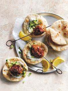 three small pita sandwiches on a plate with lemon wedges