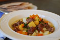 a white bowl filled with meat and vegetables on top of a table next to crackers