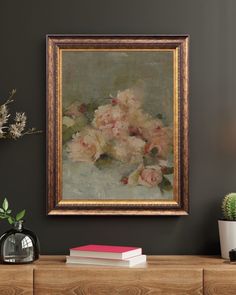 a painting is hanging on the wall above a dresser with books and flowers in it