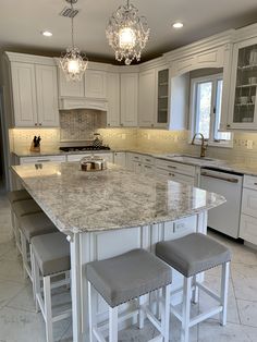 a large kitchen with marble counter tops and white cabinets, two stools at the island