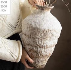 a woman is holding a vase with twigs in it