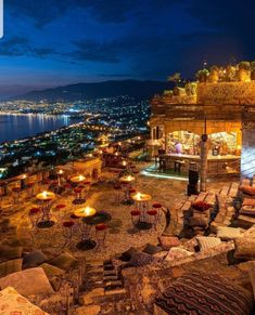 an outdoor seating area with tables and chairs overlooking the city lights at night, lit up by candles