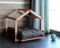 a dog bed in front of a window next to a green ball on the floor