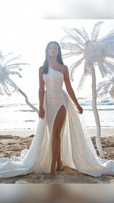 a woman standing on top of a sandy beach next to the ocean wearing a white dress