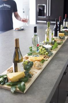 a man standing in front of a counter filled with wine bottles and cheese on it