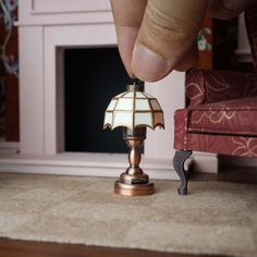 a miniature lamp is on the floor in front of a fire place with a person's finger pointing at it