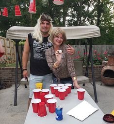 a man and woman standing next to each other at a table with cups on it