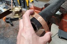 a hand holding a piece of metal in the middle of a workbench with tools nearby