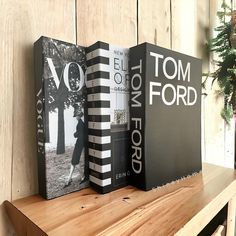 three books sitting on top of a wooden shelf next to a potted pine tree