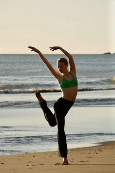 a woman doing yoga on the beach with her arms in the air and one leg up