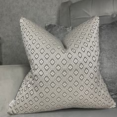 two pillows sitting on top of a bed next to a pillow case with an intricate design