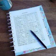 a notebook with a pen on top of it next to a cup and coffee mug