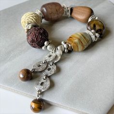 "Vintage Chico's earthy mixed bead bracelet, with dangling charms. Very chunky nuetral tone bracelet comprised of agate, tiger's eye, wood, coir, nut, resin and matte silver tone beads.  The bracelet is made in the USA and NOS (new old stock). This is a stretch bead bracelet that should fit medium sized wrists. The original price tag is $34. Measurements: Size medium The beads vary in size - the banded agate is 1 1/8 x 3/4\"  Total weight is 82 grams Condition: Very good with no noticeable wear. Artisan Brown Bracelets With Gemstone Beads, Artisan Brown Bracelet With Gemstone Beads, Brown Beaded Bracelets With Natural Stones, Earthy Brown Beaded Bracelets With Gemstone Beads, Earthy Brown Bracelets With Gemstone Beads, Earthy Brown Gemstone Beads Bracelets, Earthy Brown Beaded Bracelets With Large Beads, Bohemian Brown Stretch Bracelet For Healing, Nature-inspired Brown Beaded Bracelets With Natural Stones