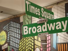 two green street signs sitting on top of a metal pole in front of a wall