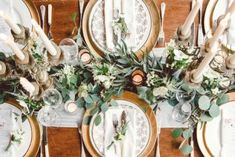 the table is set with plates, silverware and greenery