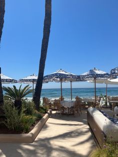 an outdoor dining area with tables and umbrellas on the beach near the water's edge