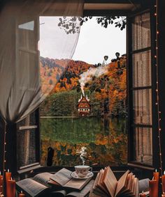 an open book sitting on top of a wooden table next to a window filled with books