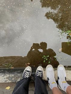 two people standing next to each other in front of a puddle with their feet on the ground