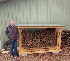 a man standing in front of a pile of firewood next to a green building