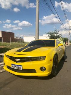 a yellow chevrolet camaro is parked on the side of the road with power lines in the background