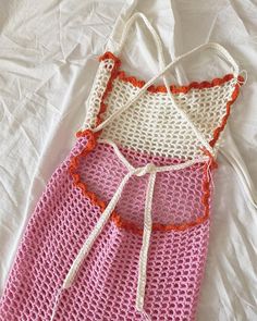 a pink and white crocheted dress with an orange trim on the bottom, sitting on top of a bed