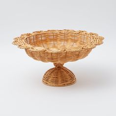 a wicker bowl on a stand with no handles, sitting on a white surface