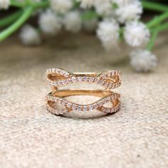 two gold rings with white diamonds on top and one in the middle, sitting next to some flowers