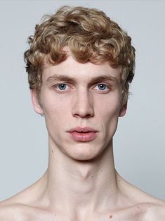 a man with curly hair and blue eyes is posing for the camera in front of a white background