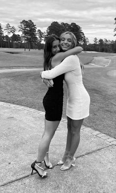 two young women hugging each other on the sidewalk in front of a golf course, black and white photo