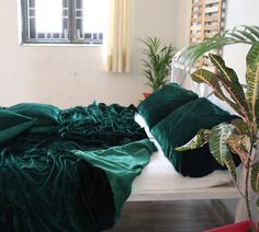 a bed with green sheets and pillows on top of it next to a potted plant