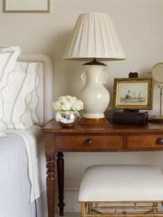 a white lamp sitting on top of a table next to a wooden dresser and chair