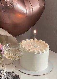 a birthday cake with a lit candle on it next to a wine glass and some balloons