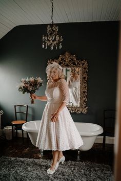 a woman standing in front of a bathtub with flowers on the floor and holding a bouquet