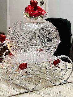 a clear glass carriage with red roses on it's top and wheels, sitting on a wooden table