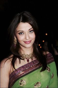 a woman in a green and gold sari with jewels on her neck posing for the camera