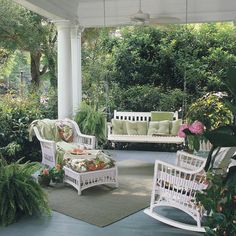 a porch with white furniture and lots of greenery