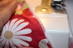 a person is sewing on a red and white flowered fabric