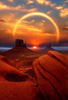 the sun is setting over some rocks in the desert with an arch and rock formations