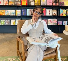 a woman sitting in a chair reading a book with her hand on her chin and looking at the camera